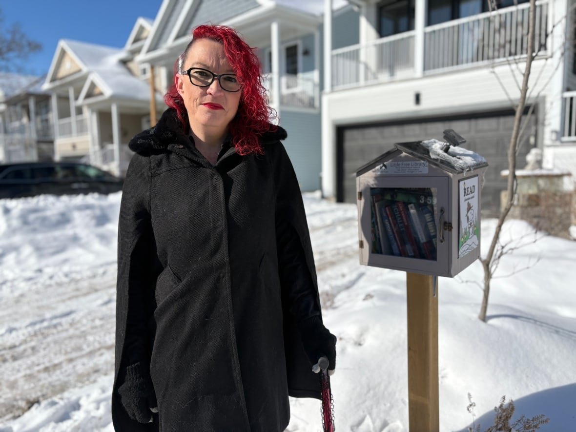 christine-young Woman with red hair stands next to little library box.