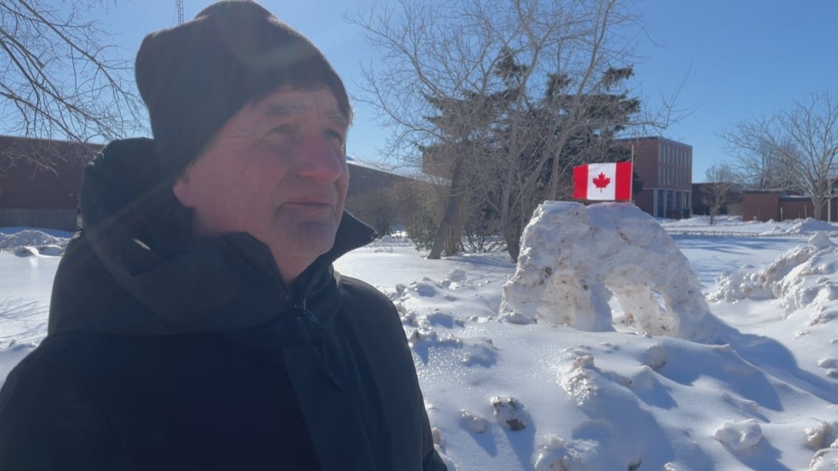 christopher-griffin-on-flag-day Man wearing black tuque and jacket stands in front of an elephant sculpture made of snow with a Canadian flag flying above it.