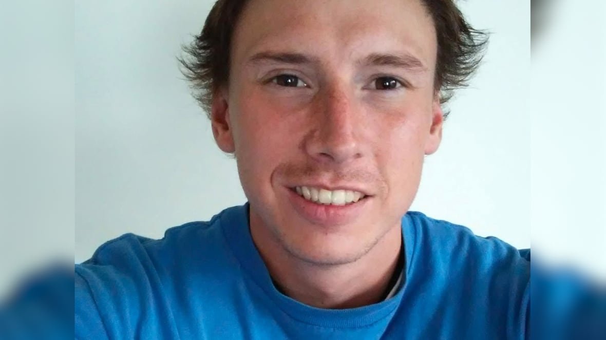 A young man in a blue T-shirt looks into the camera.