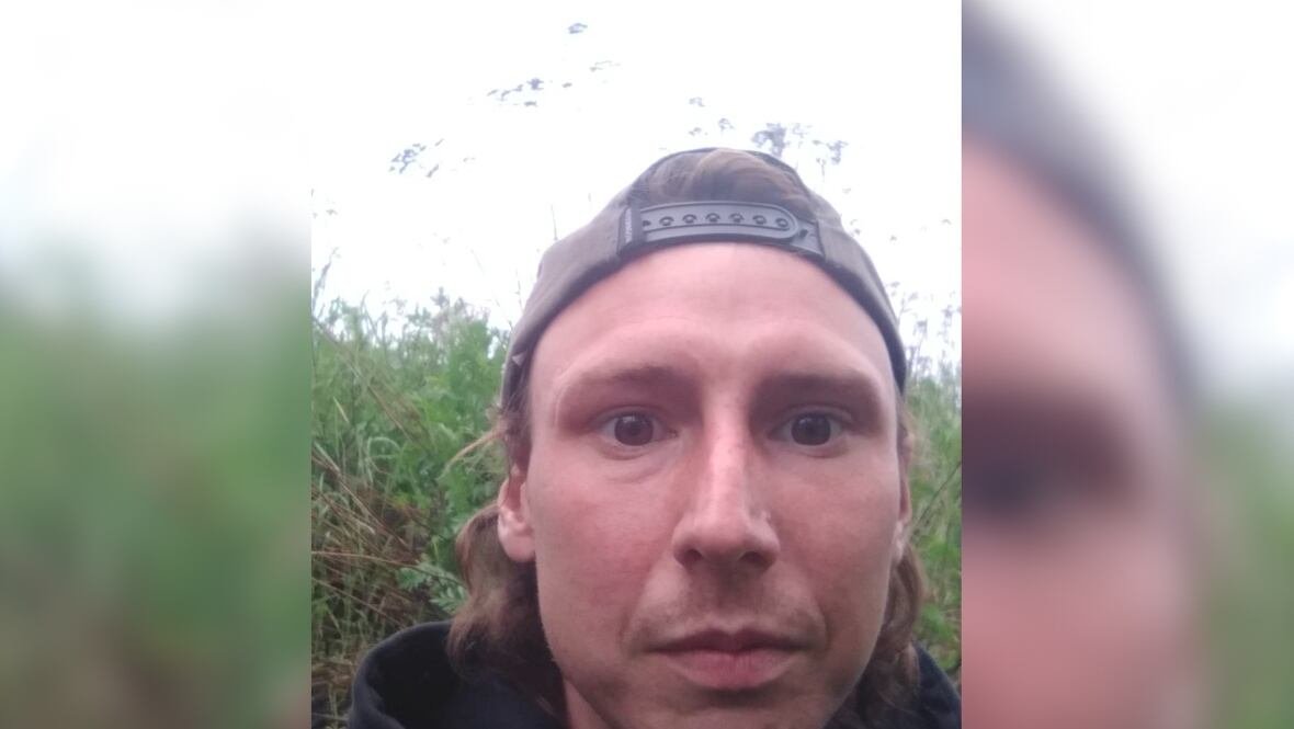 A young man takes a photo of himself outside, while wearing a backwards baseball cap.