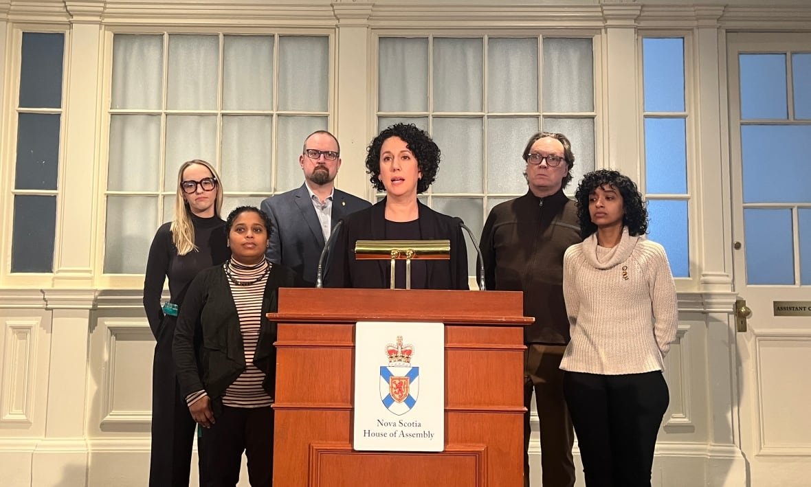 A woman stands at a podium with people standing to either side of her.