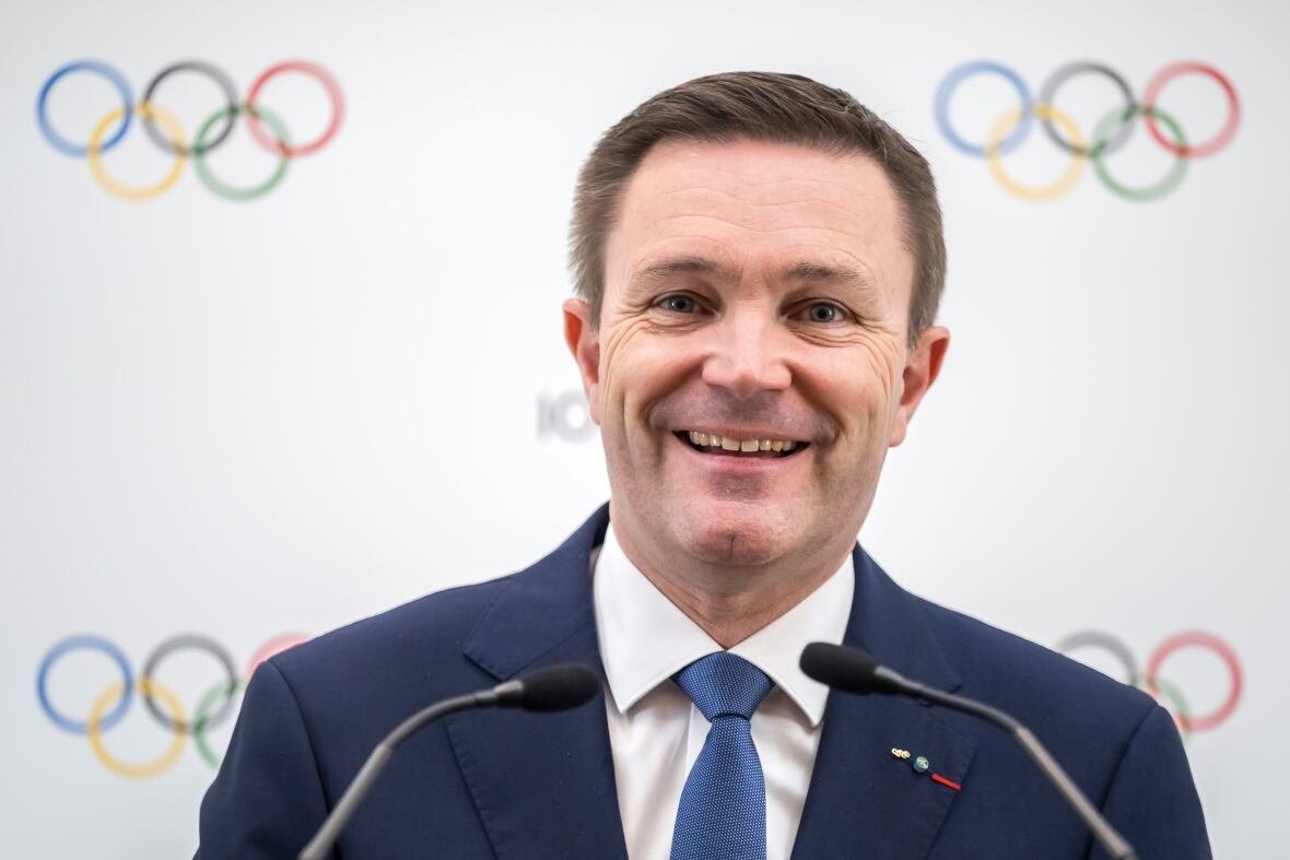 david-lappartient A man smiles in front of a white background with the Olympic rings on it.