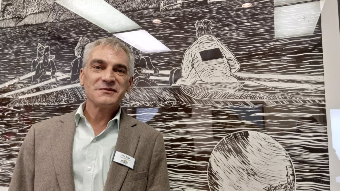 destination-st-john-s-ceo-paul-bugge Man in grey suit standing against a black and white drawing.