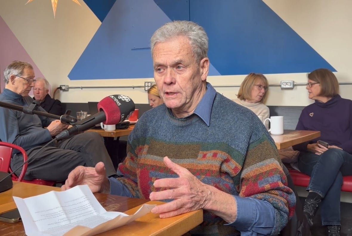 doug-jones-voter-in-cambridge-1 Man sitting at a table in a coffee shop with a CBC microphone in front of him