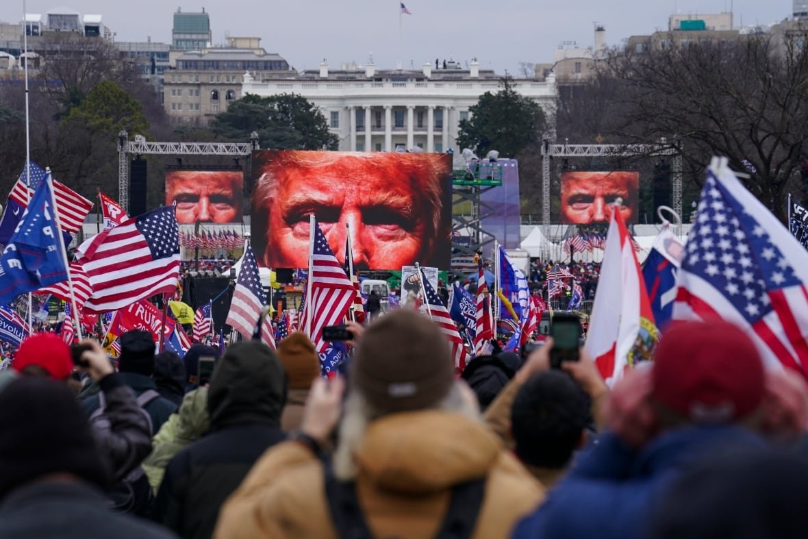 election-2024-trump-insurrection-amendment Trump supporters participate in a rally in Washington holding pictures of Trump and American flags.