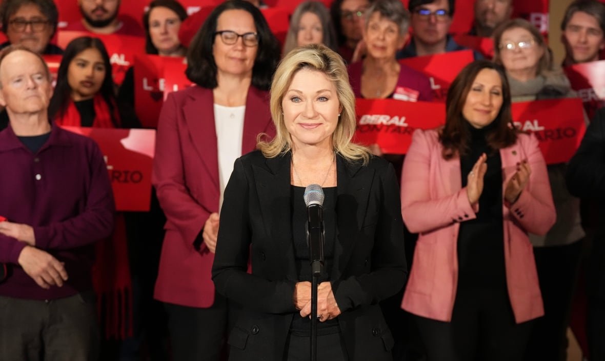 elxn-ont-20250221 Bonnie Crombie stands at a microphone with a group of her candidates and supporters in the background.