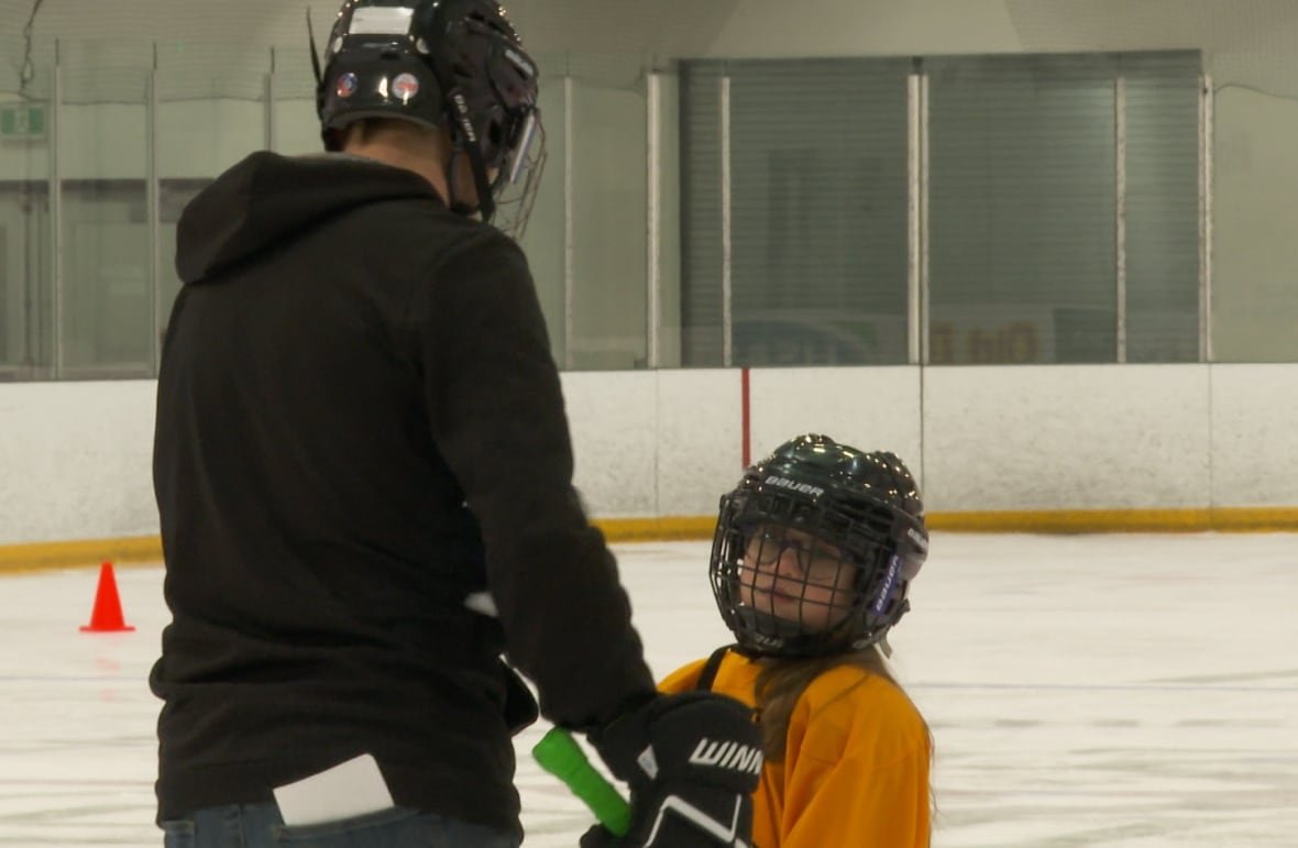A young hockey player in a yellow jersey is talked to by an adult.
