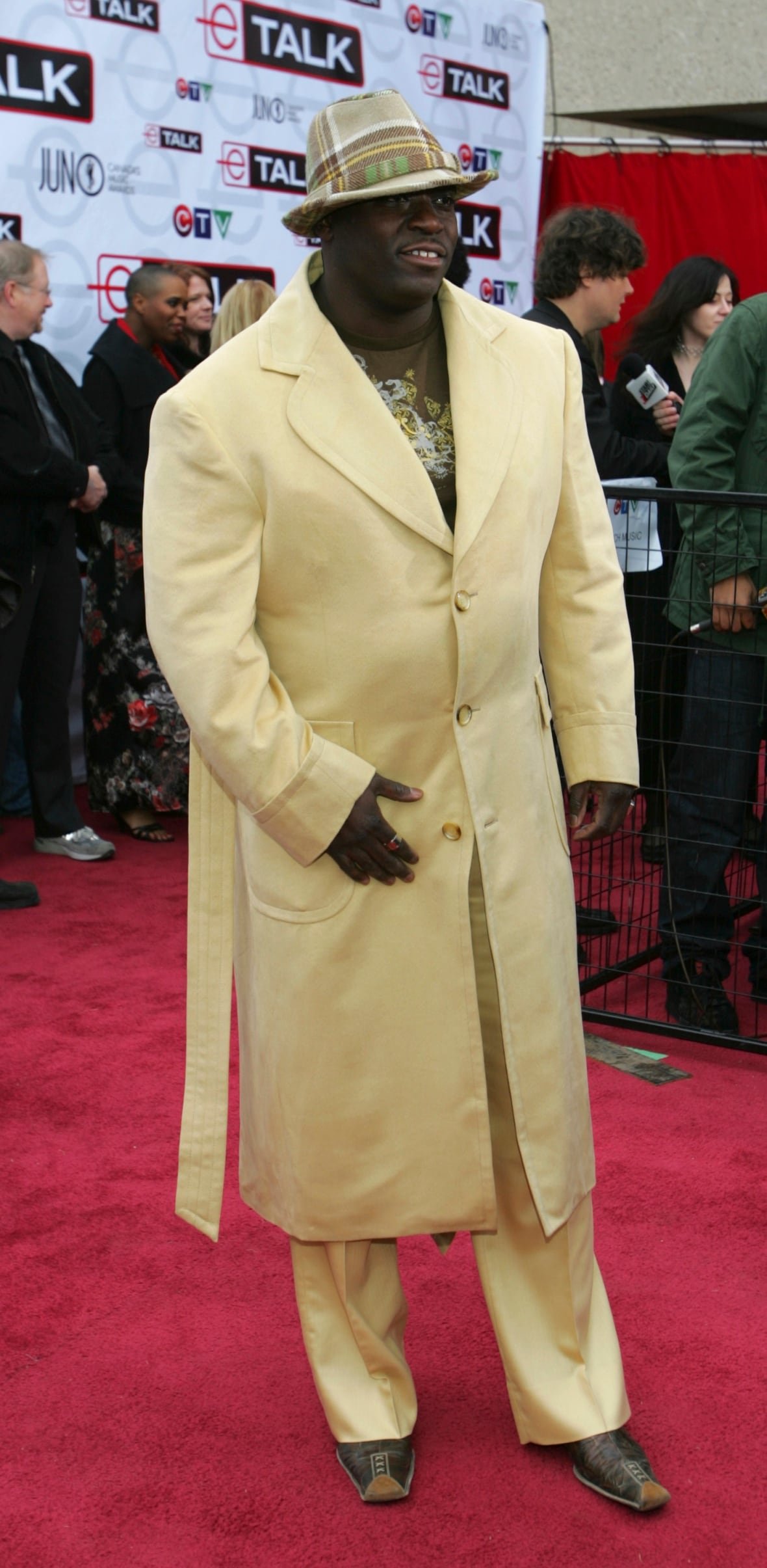 Farley Flex on the red carpet wearing light yellow pants with a matching long coat and a plaid hat.