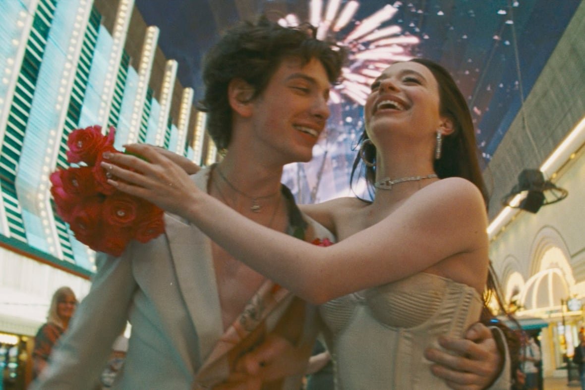 film-review-anora A smiling man and woman embrace. Behind them are neon lights and fireworks.