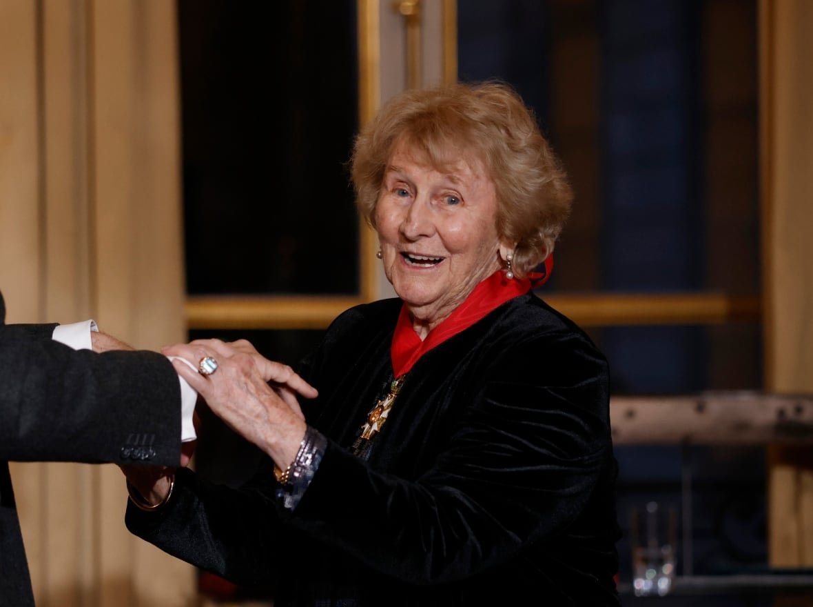 A smiling elderly woman shakes a man's hand.