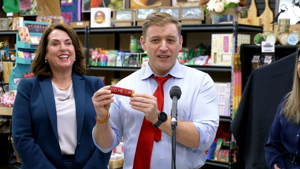 Man in suit holds red choclate bar that says 'Kiss me, luh.'