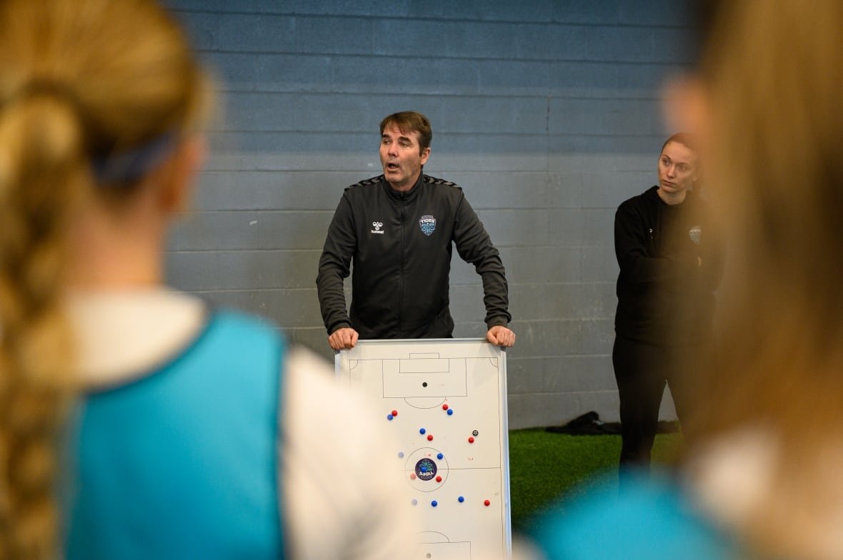 halifax-tides-fc A man holds up at a white board as he speaks to a room of athletes.
