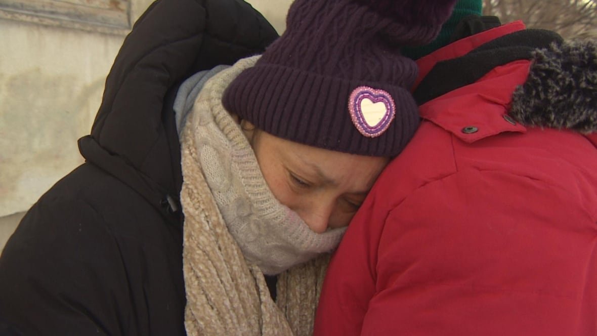 helen-mcleod A woman in winter gear resting her head on the shoulder of a man outdoors.