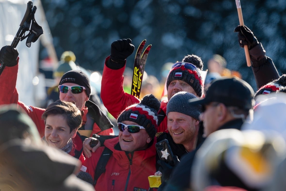 invictus-games-20250211 Several people wearing winter clothes smile for a photo. Some are holding skis and ski poles.