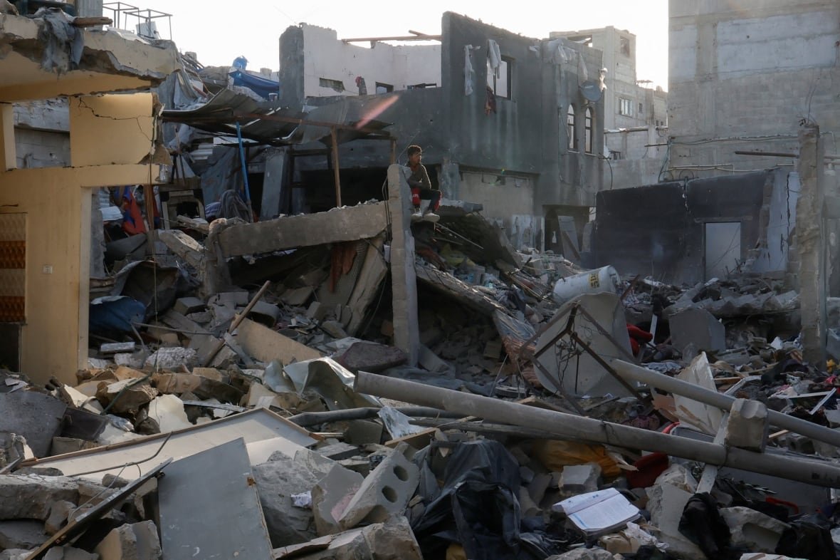 israel-palestinians-gaza-2 A small boy sits atop rubble as a mass of concrete debris is shown in an urban setting.