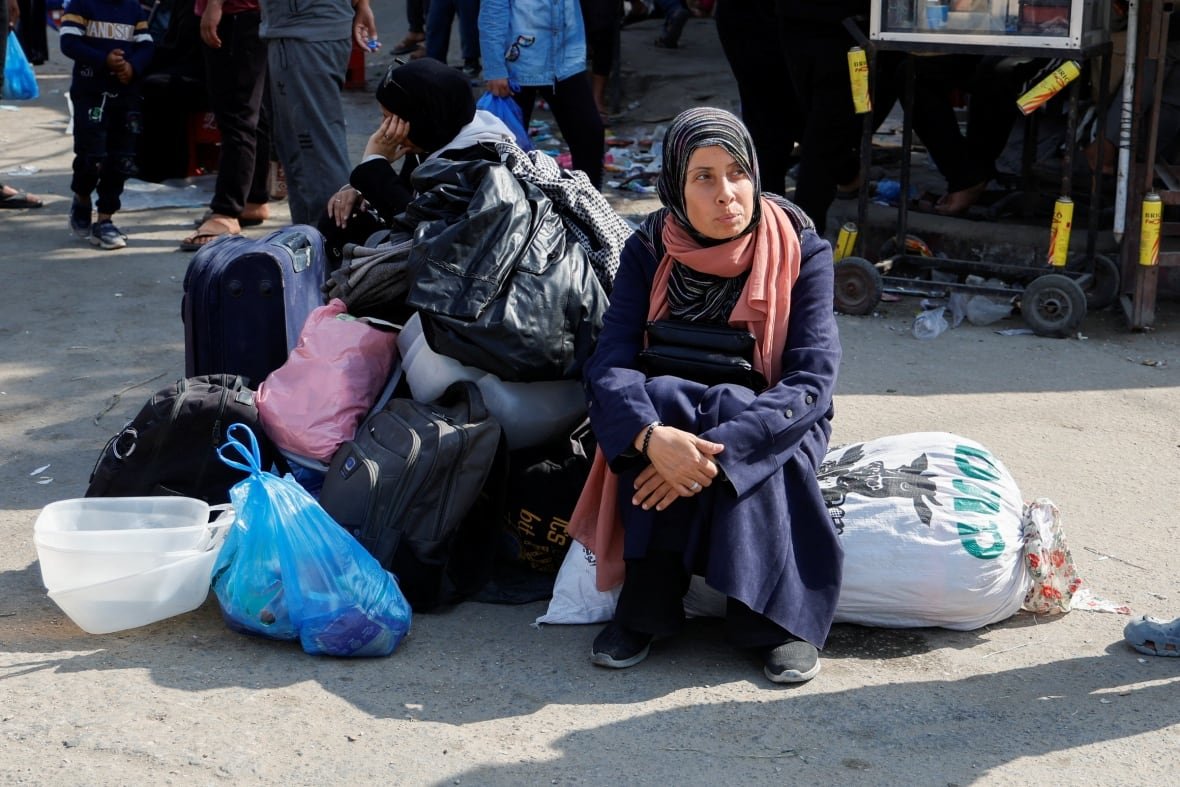 israel-palestinians-gaza-3 A woman in a head covering sits beside a number of suitcases, bags and a garbage bag.