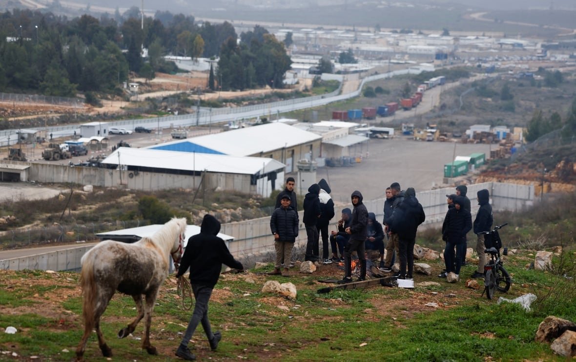 People gather atop a hill that overlooks a prison complex.