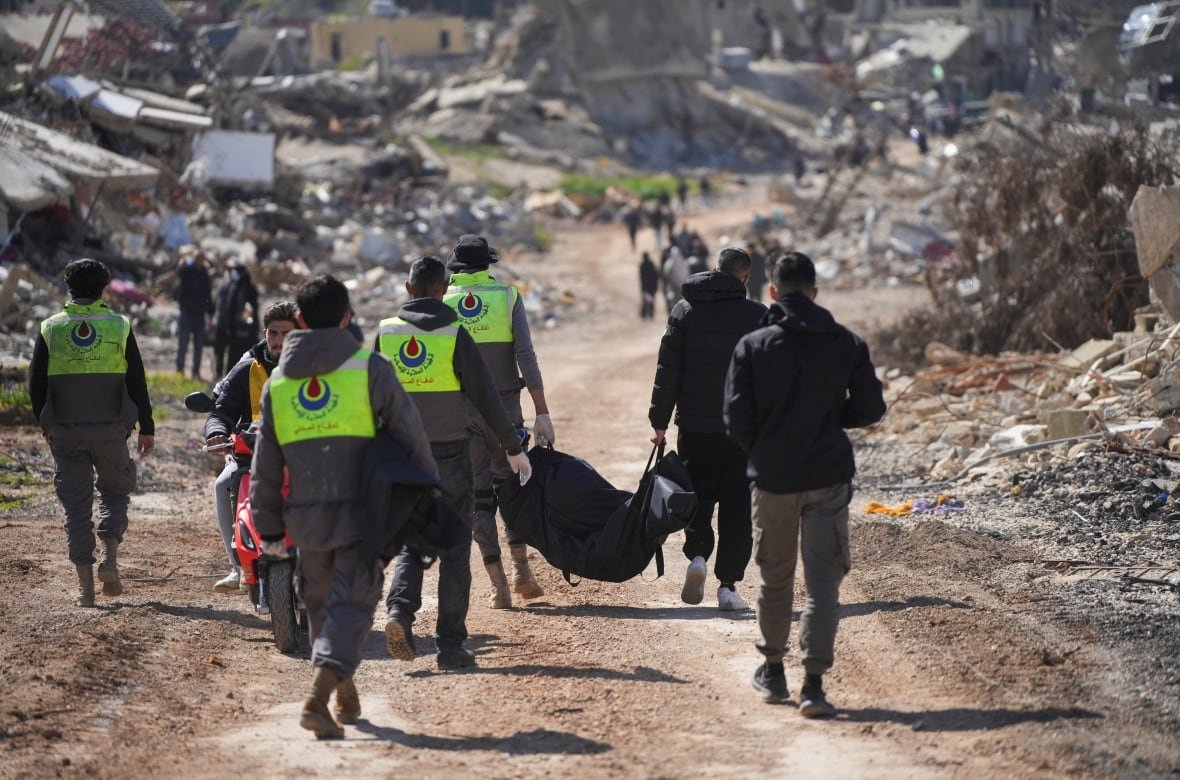 israel-palestinians-lebanon-withdrawal-1 People walk alongside rubble as they carry a body in a bag.