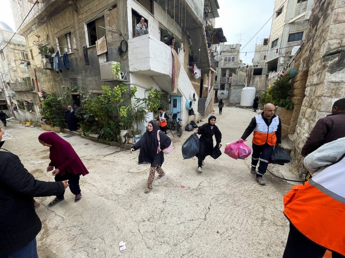 israel-palestinians-west-bank-tulkarm A group of people walk along a road carrying their belongings.