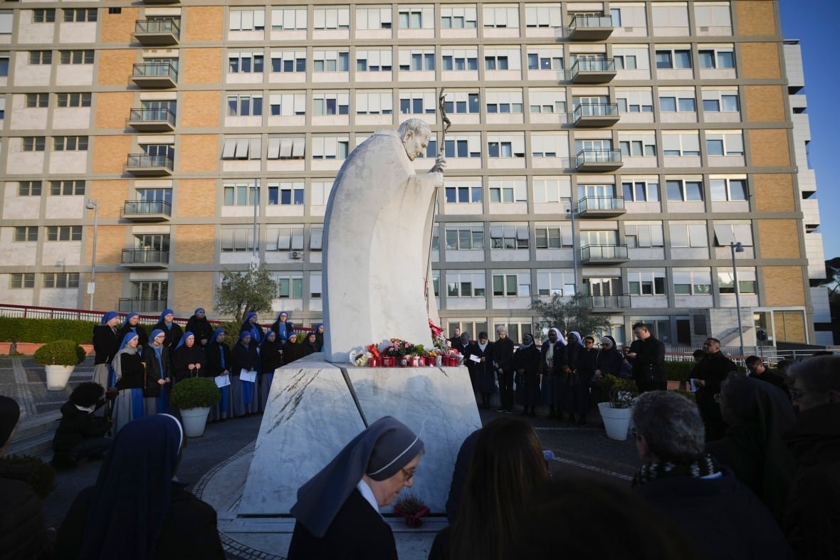 Nuns and priests gather around a statue during a vigil.