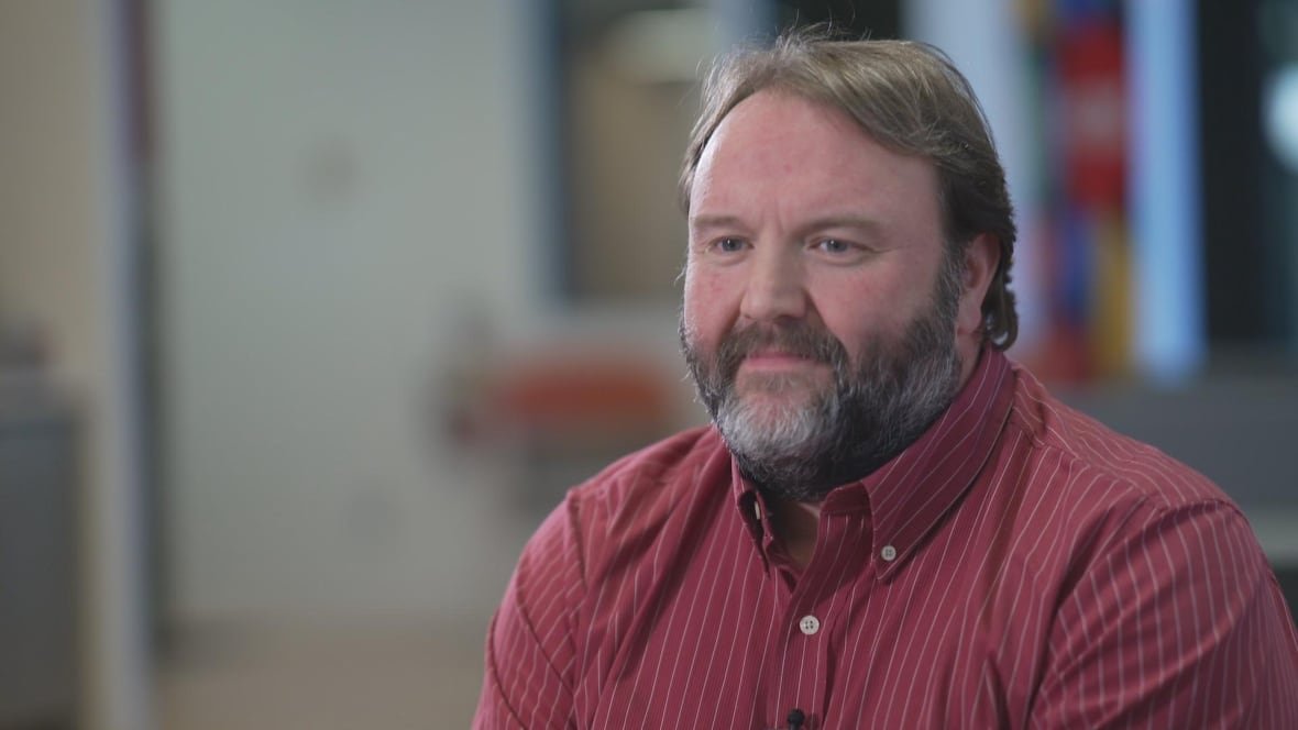 A man with a beard sits in an office.