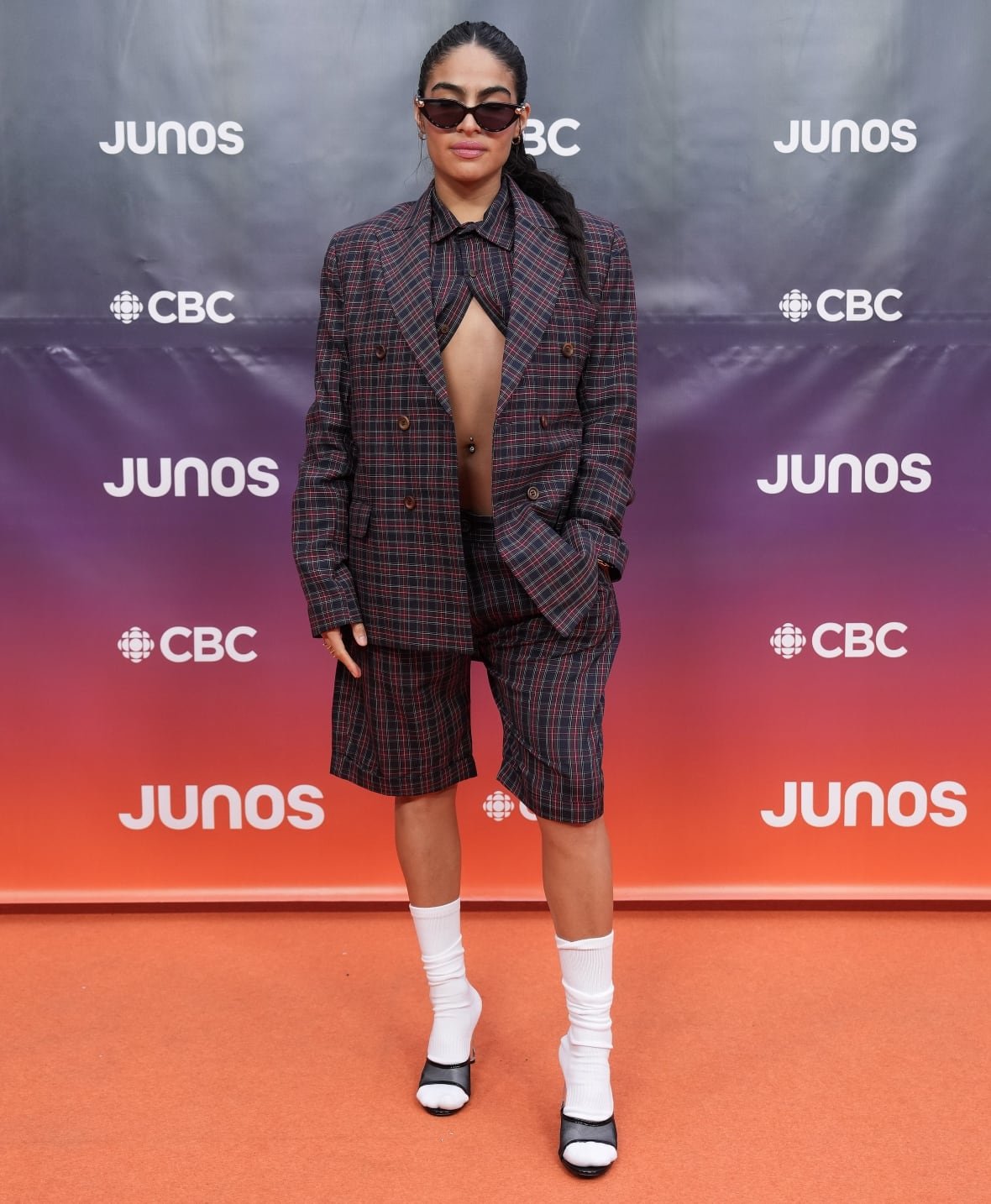 Jessie Reyez on the red carpet wearing a plaid blazer and matching, long shorts.