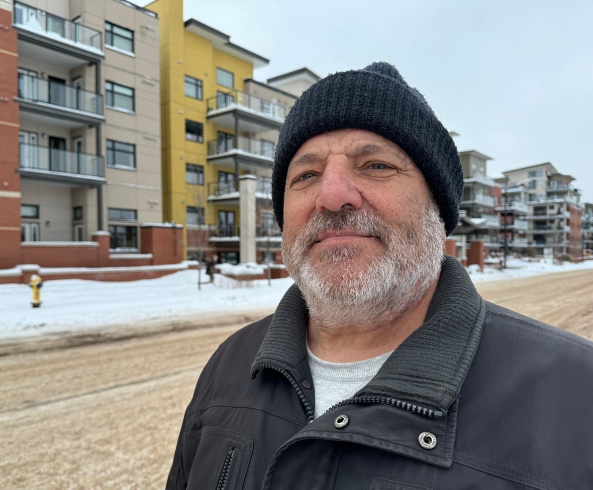 jim-carey-life-lease A man wearing a black toque stands outside in front of an apartment building during winter.