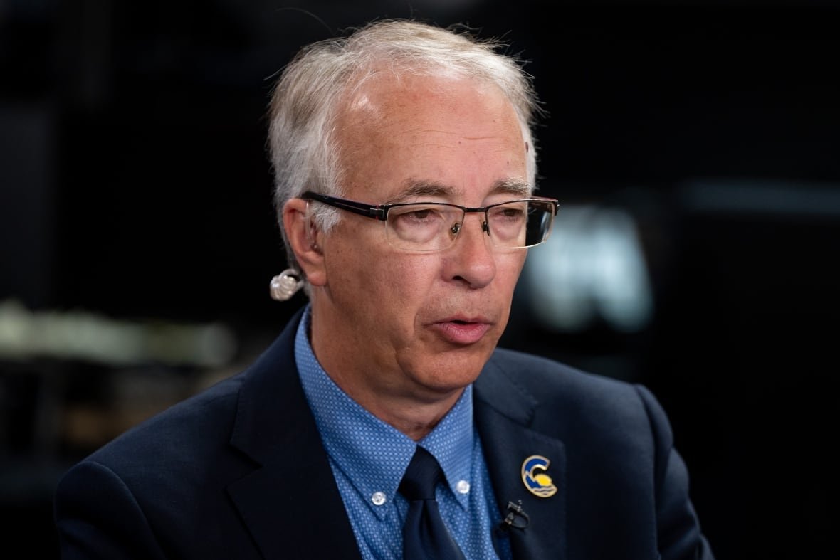john-rustad A white-haired man wearing glasses and a blue suit with a 'C' pin on it is pictured talking.