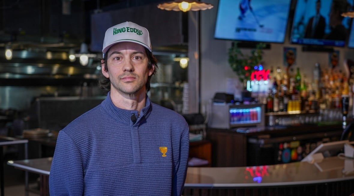 A white man in a blue sweater and a baseball cap