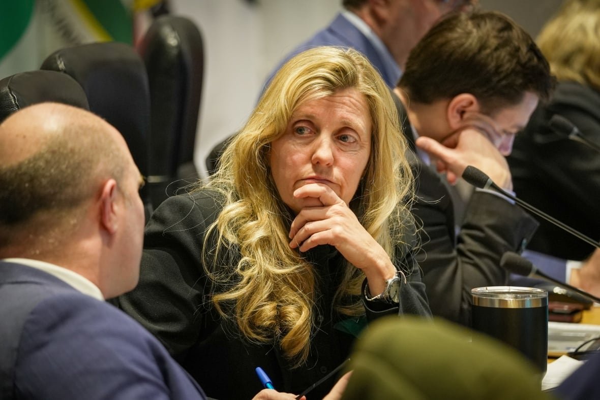 A woman with long blonde hair rests her chin on her hand