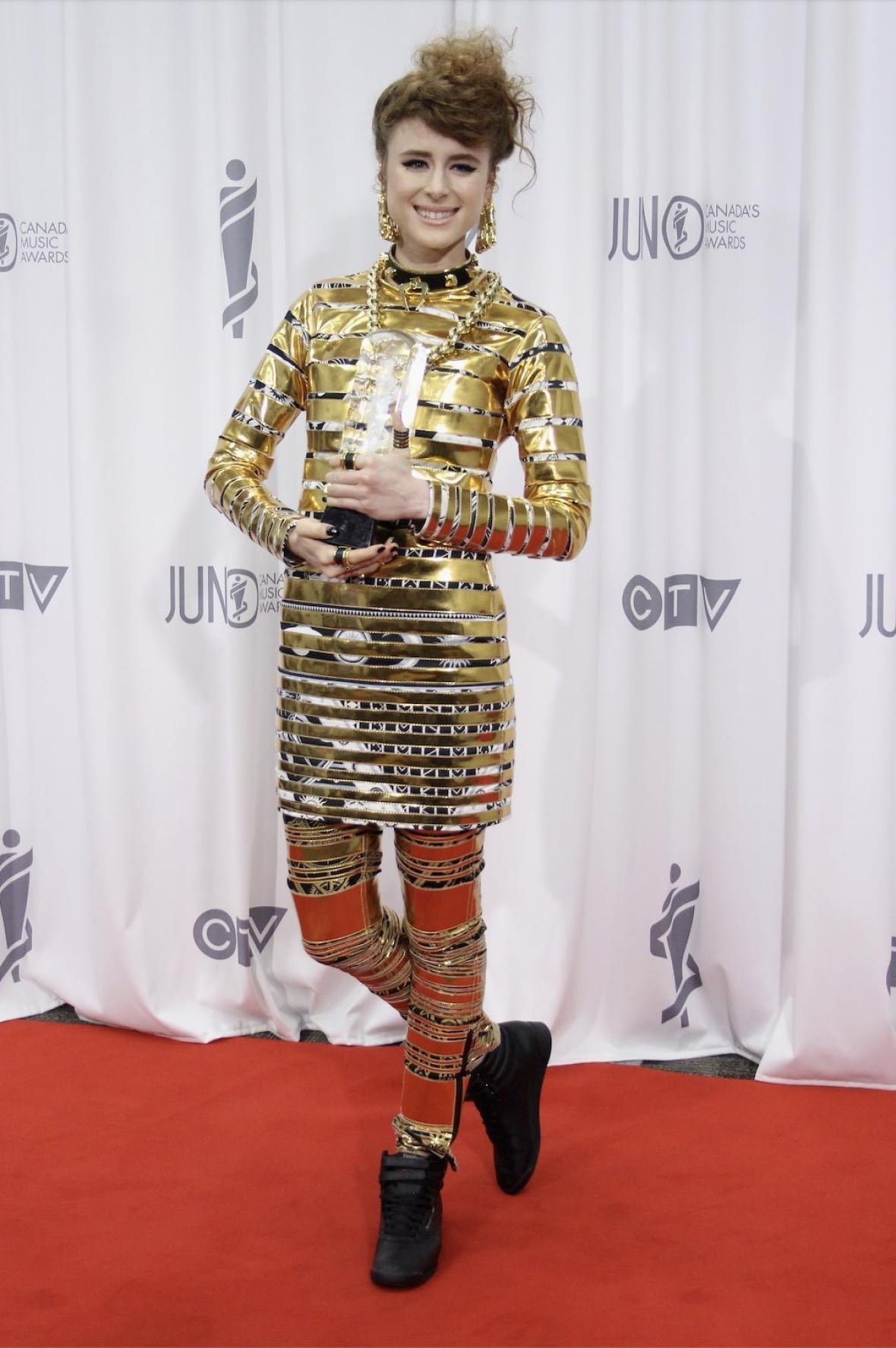 Kiesza on the red carpet wearing a gold dress, gold pants and black sneakers.