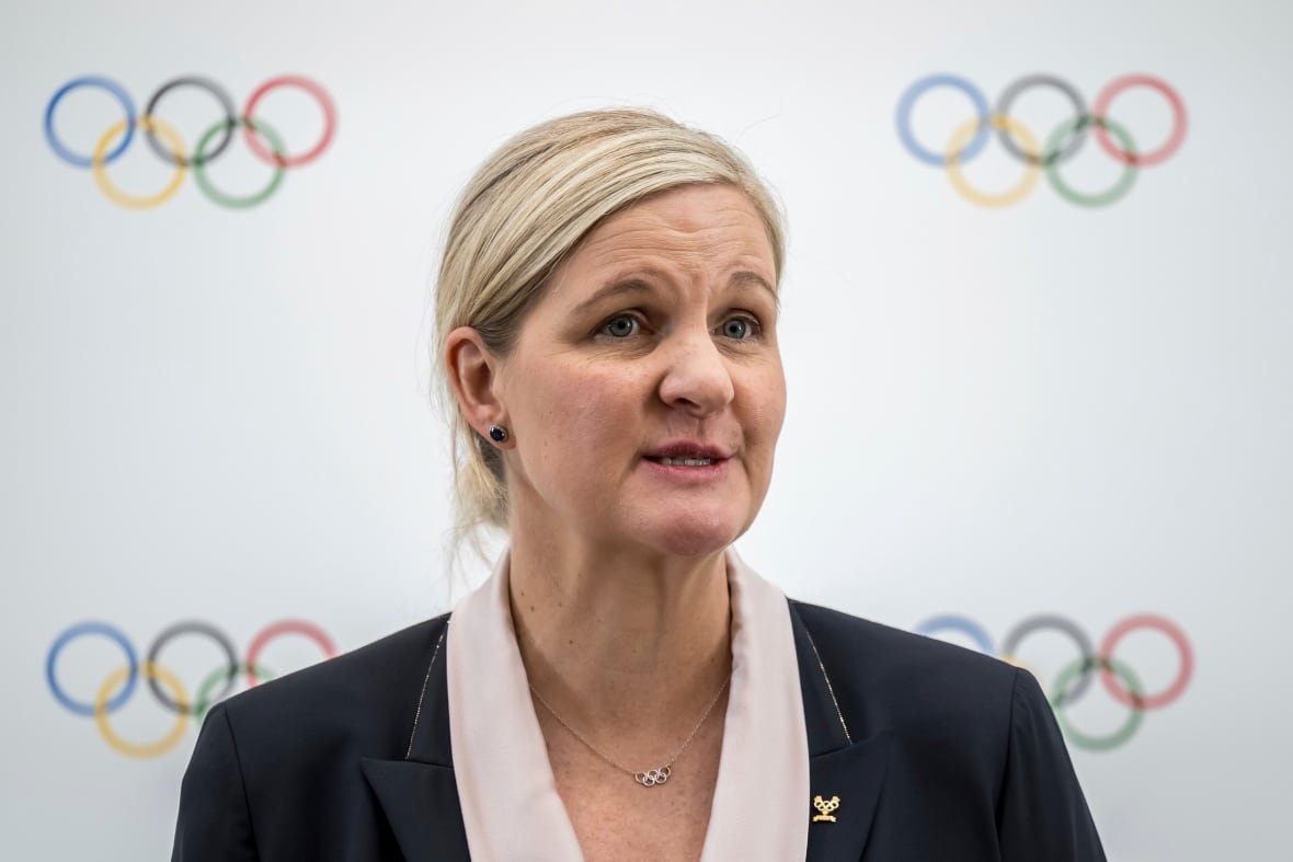 kirsty-coventry A woman speaks, with the Olympic rings on a white background behind her.