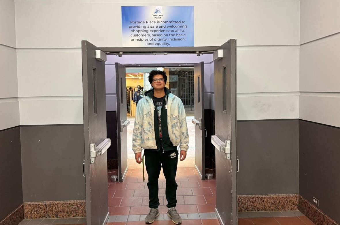 lead-navigator-josh-nepinak A young man wearing a green sweat suit and grey shoes stands under a doorway at a mall