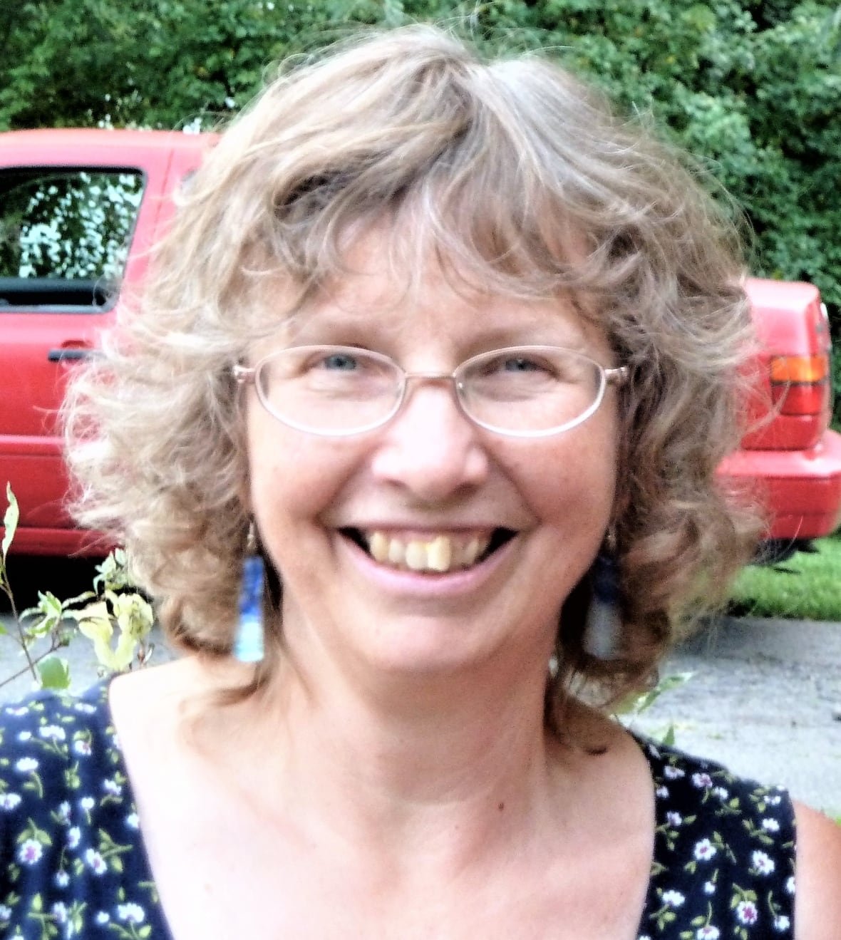 marilyn-manzer A woman smiles for the camera, with foliage and a truck visible behind her.