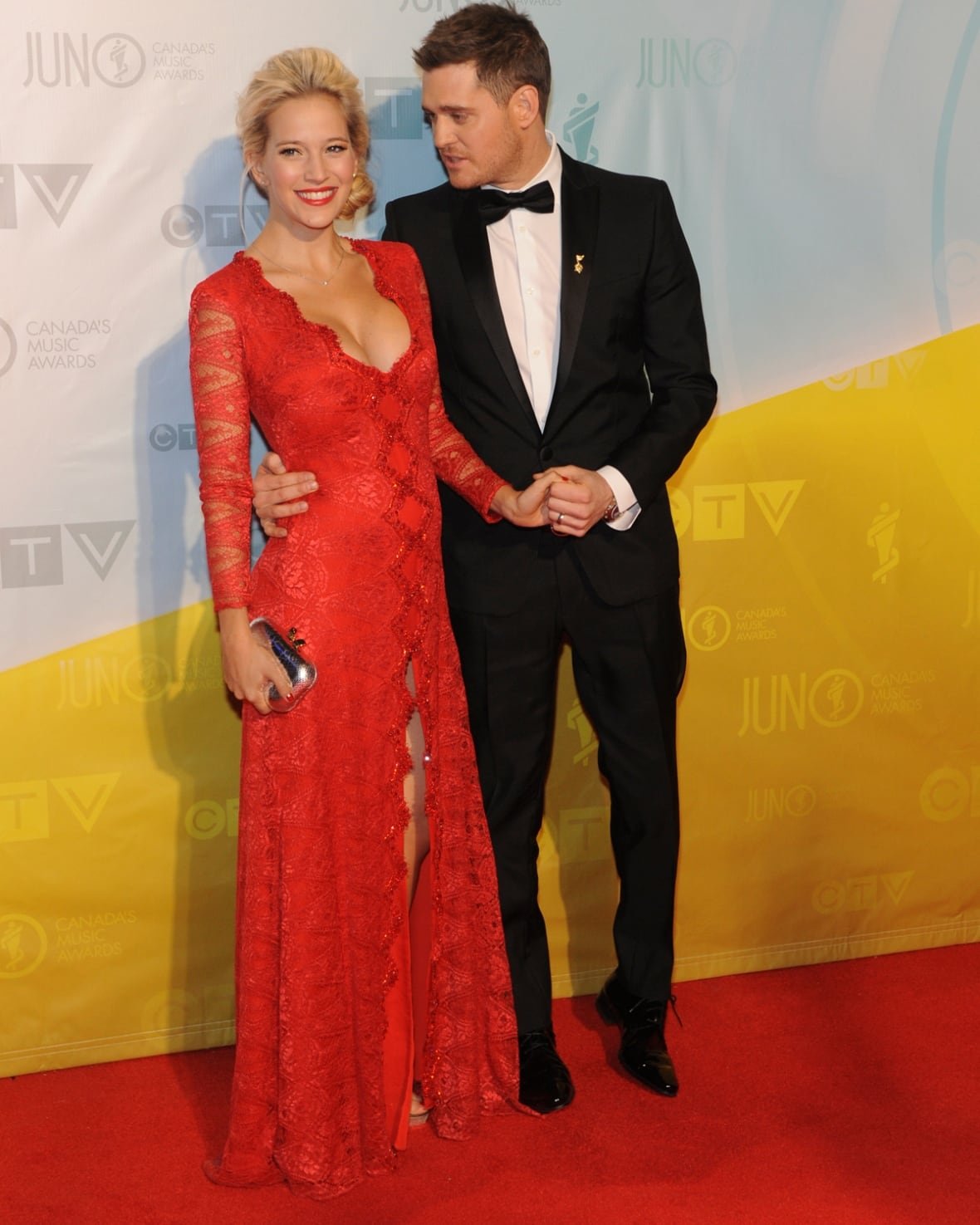 Michael Bublé and Luisana Lopilato on the red carpet wearing a black tux and a red lace dress.
