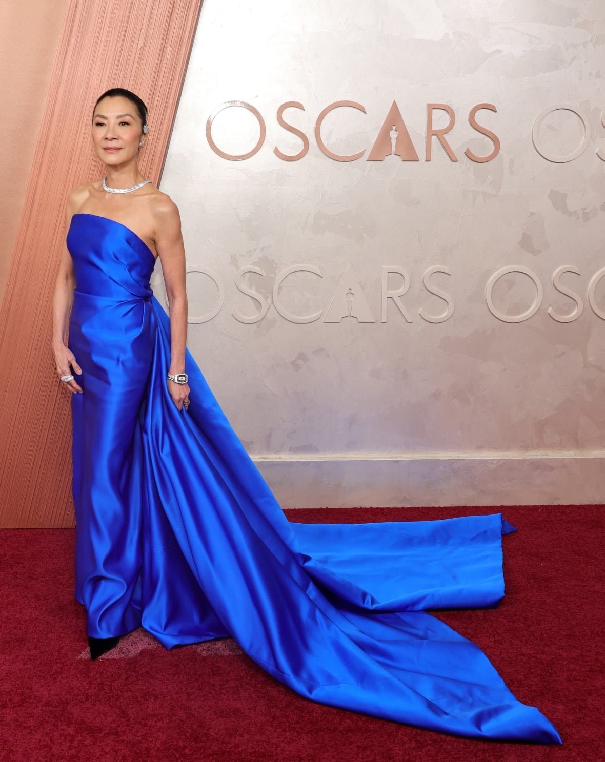 michelle-yeoh-attends-the-97th-annual-oscars-at-dolby-theatre Michelle Yeoh on the red carpet wearing a bright blue, strapless column dress with a long train.
