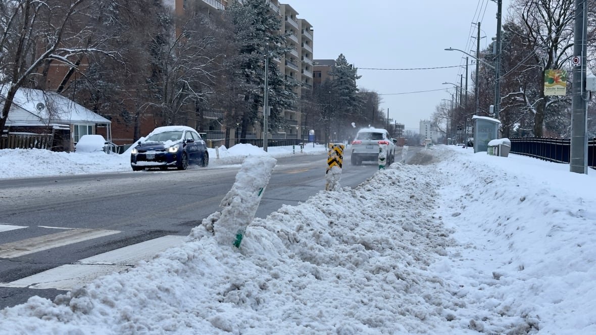 A bike lane on a city street is filled with snow. Two snow-covered cars drive by.