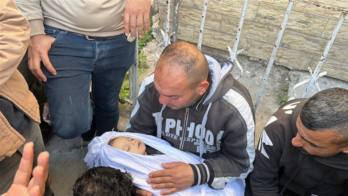 GRAPHIC - A man holds a dead infant.