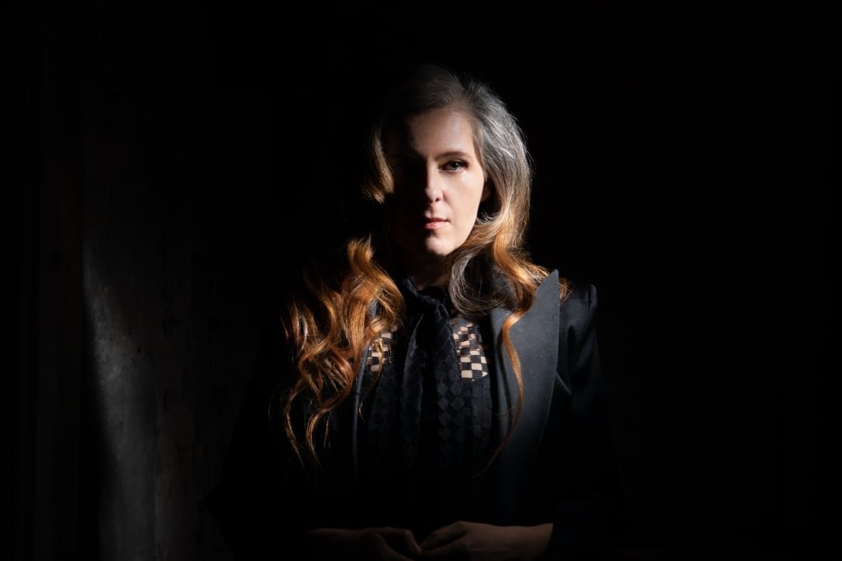 neko-case-1 A woman with long red hair stands in a shadow.