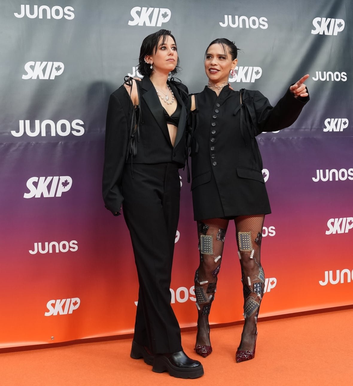2 people on the red carpet, one is wearing a black vest and pants, the other is wearing a black dress.