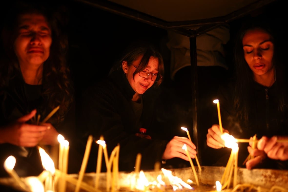 north-macedonia-nightclub-fire Three young women are shown in a nighttime photo, holding candles.