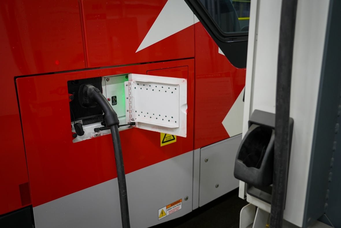 oc-transpo-electric-bus-plugged-in-to-a-charger-jan-30-2025 close up of a black charger plugged into the side of a red and white bus
