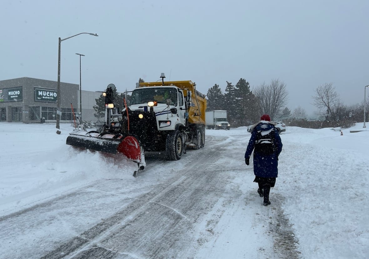 A snpwplow clears a road as a pedestrian walks on the other side.