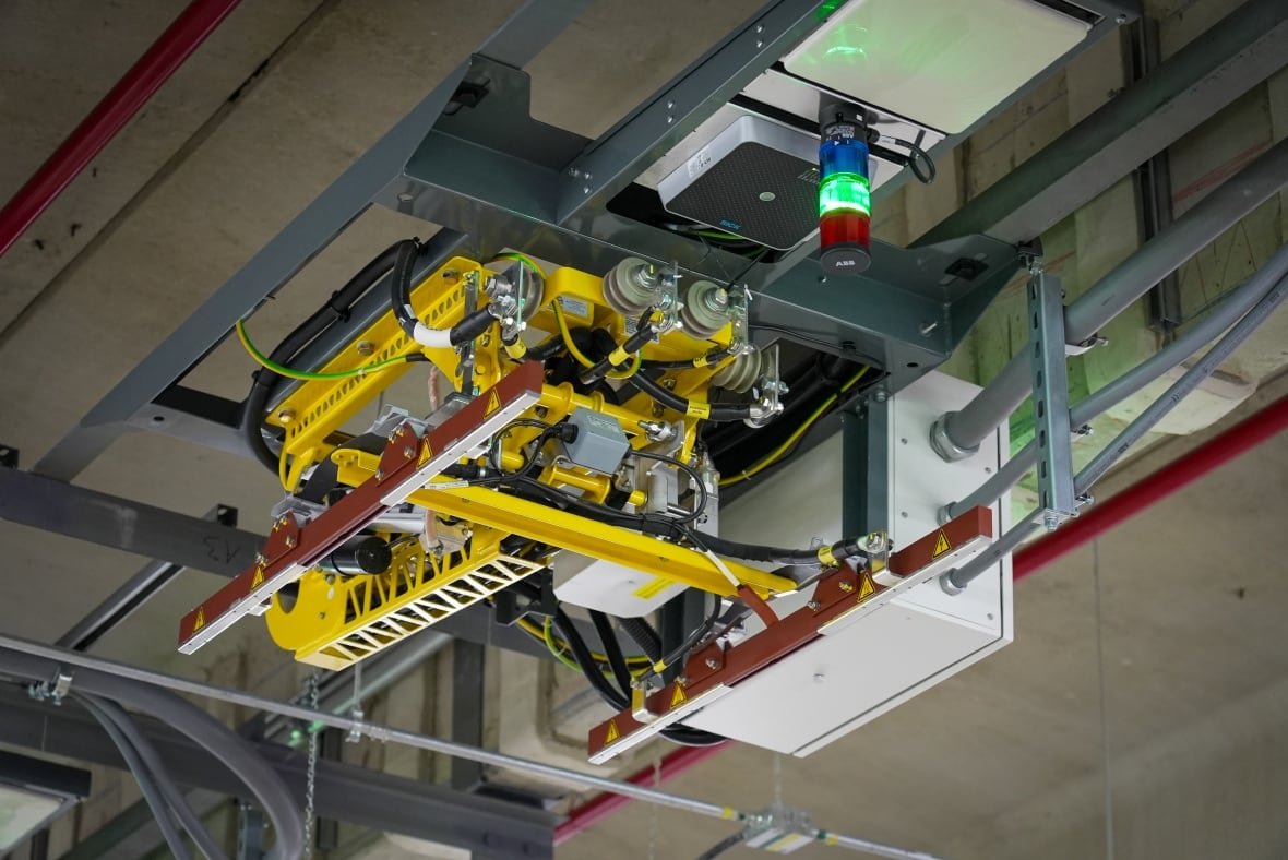 pantograph-charger-electric-bus-ebus-ottawa-oc-transpo-jan-30-2025 A yellow machine with extendable arms and a light attached to a concrete ceiling