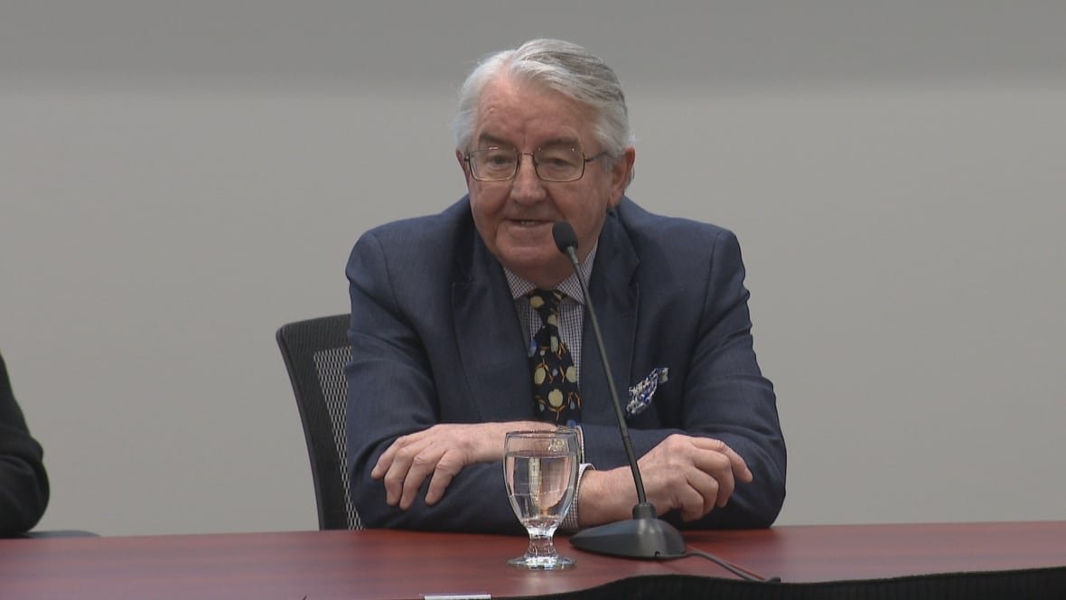 pat-parfrey-1 A man wearing a suit sits in front of a microphone on a table.