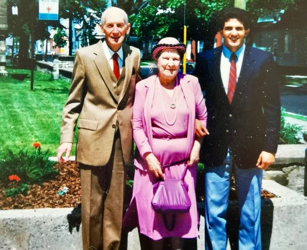 paul-hodgson-with-adoptive-parents An older man in a beige suit, left, an older woman in a pinkish-purple outfit, middle, and a younger man with a suit jacket and jeans, right.