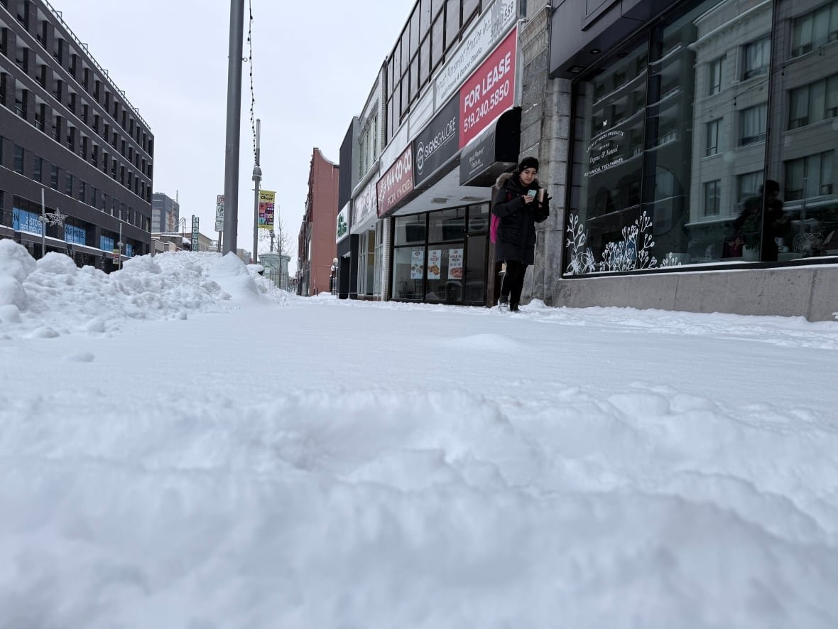A person walks on a snowy sidewalk in downtown Kitchener. The photo is taken from a lower angle to really show the snow.