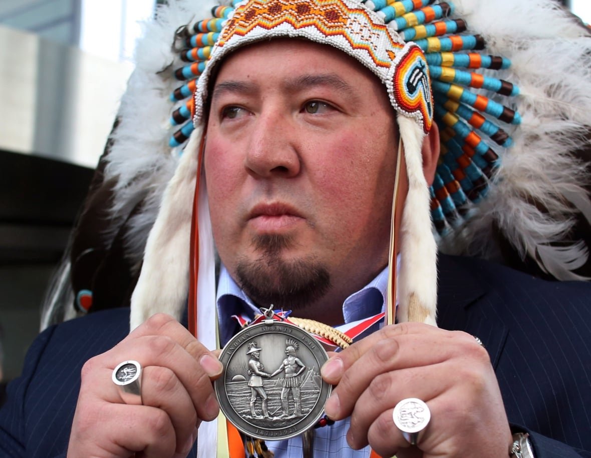 pine-creek-first-nation-chief-derek-nepinak Pine Creek First Nation Chief Derek Nepinak holds a treaty medallion while wearing a headdress.