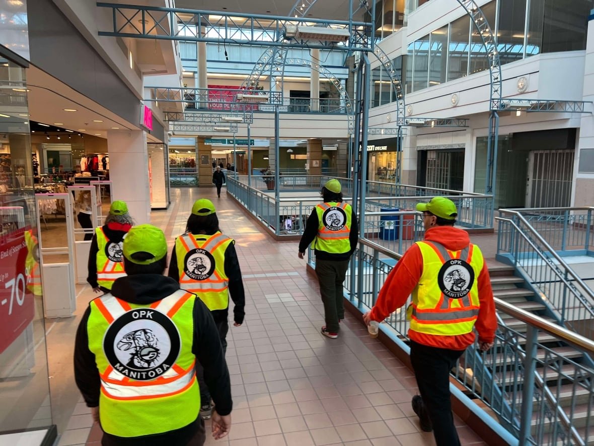 portage-place-community-helpers-making-their-rounds-of-the-mall A group of helpers wearing reflective vests and neon green hats walking in unison down the corridor of a mall hallway.