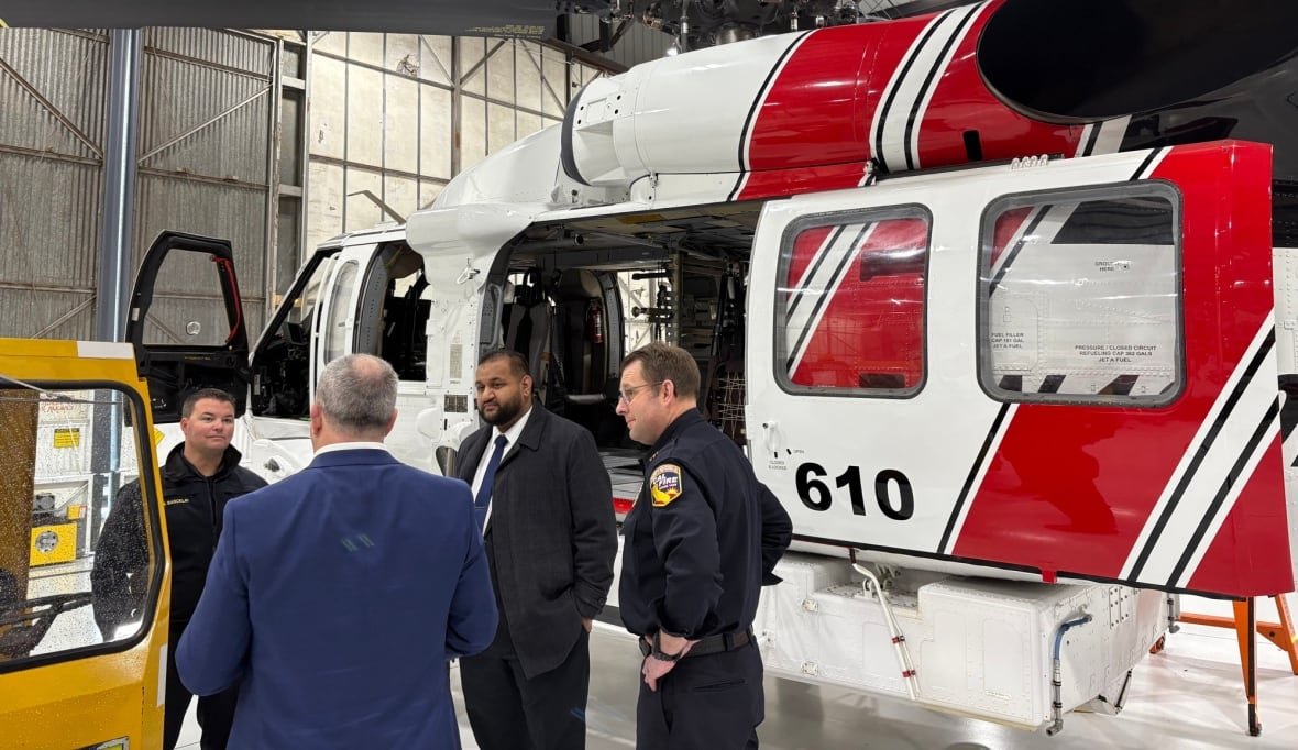 A group of people speak beside a helicopter.